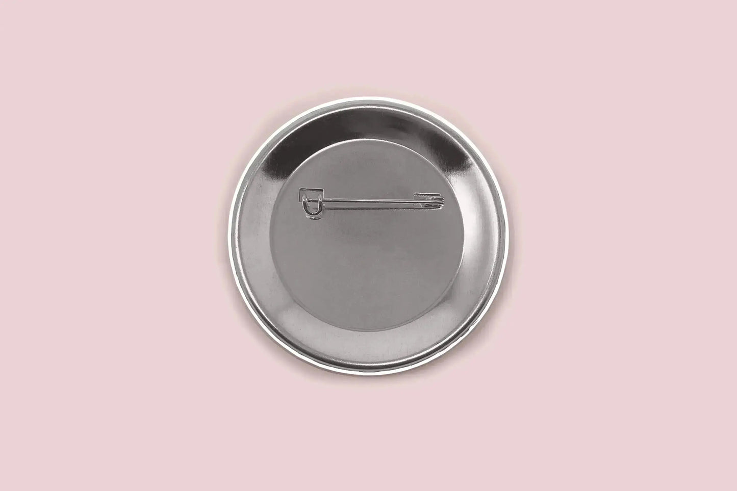 The image displays the back side of a button pin, showing the safety pin. The pin is set on a light pink background.