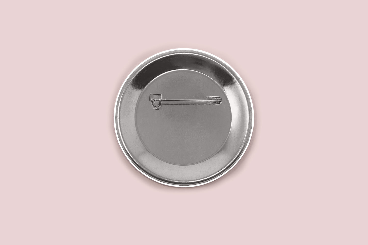 The image displays the back side of a button pin, showing the safety pin. The pin is set on a light pink background. 